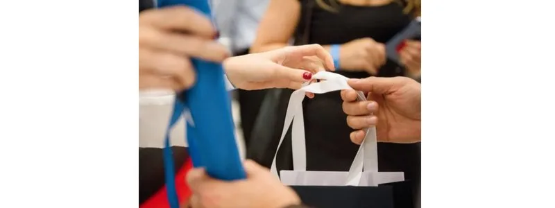 Close-up of hands exchanging a white-handled gift bag at an event.