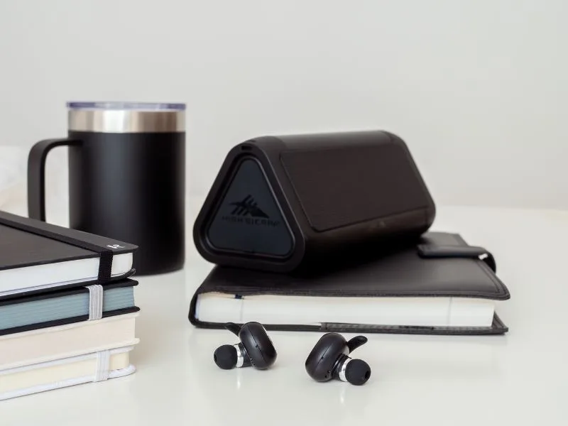 Journal Cup Speaker Black Arrangement of promotional merchandise including assorted branded journals, black speaker, ear buds and coffee cup