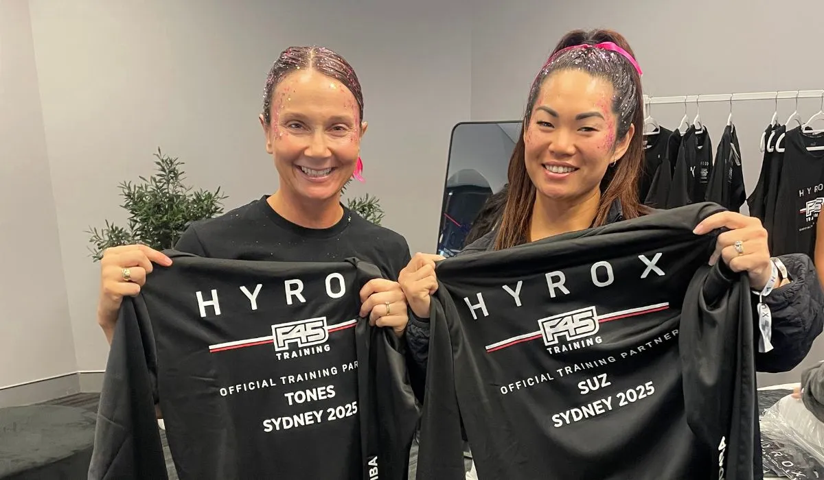 Two smiling event guests holding up personalised black t-shirts with their names printed on them at a live apparel personalisation activation.