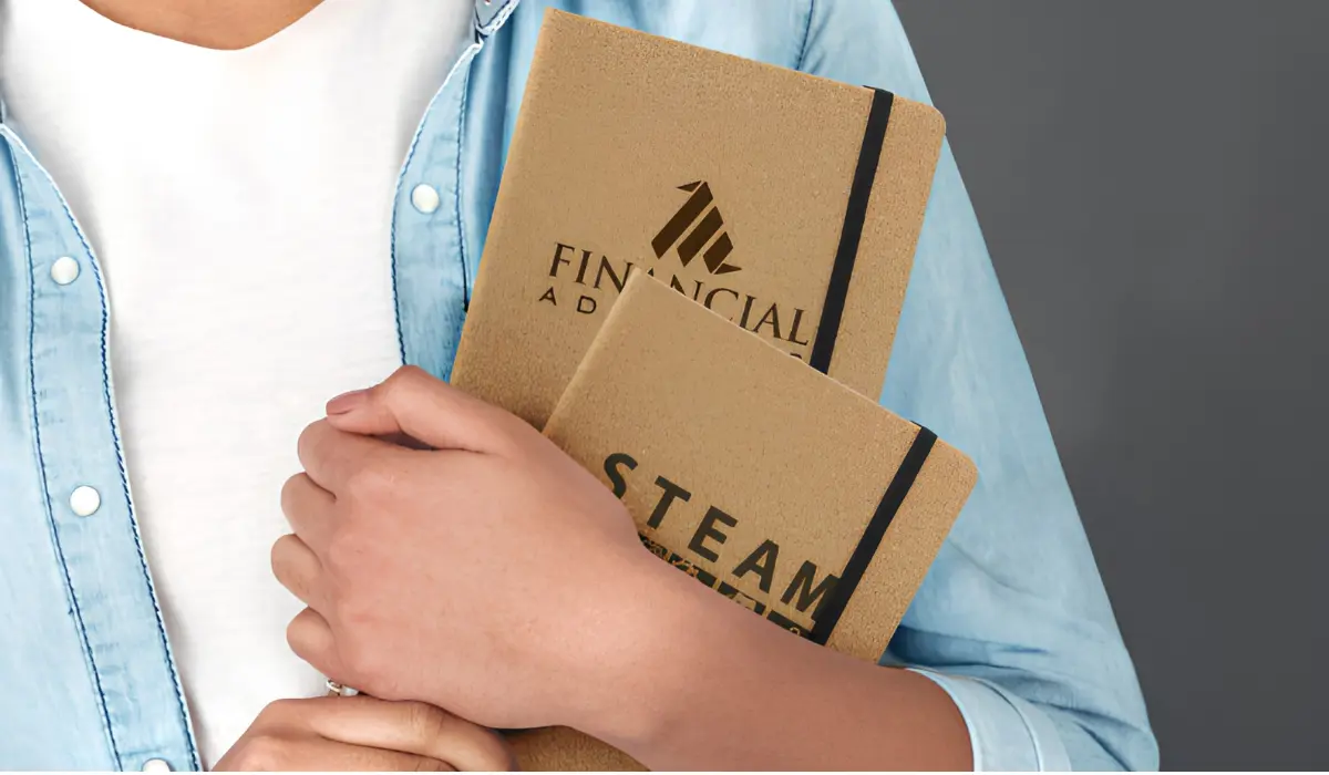 Person holding two branded kraft paper notebooks with elastic closures and custom logos