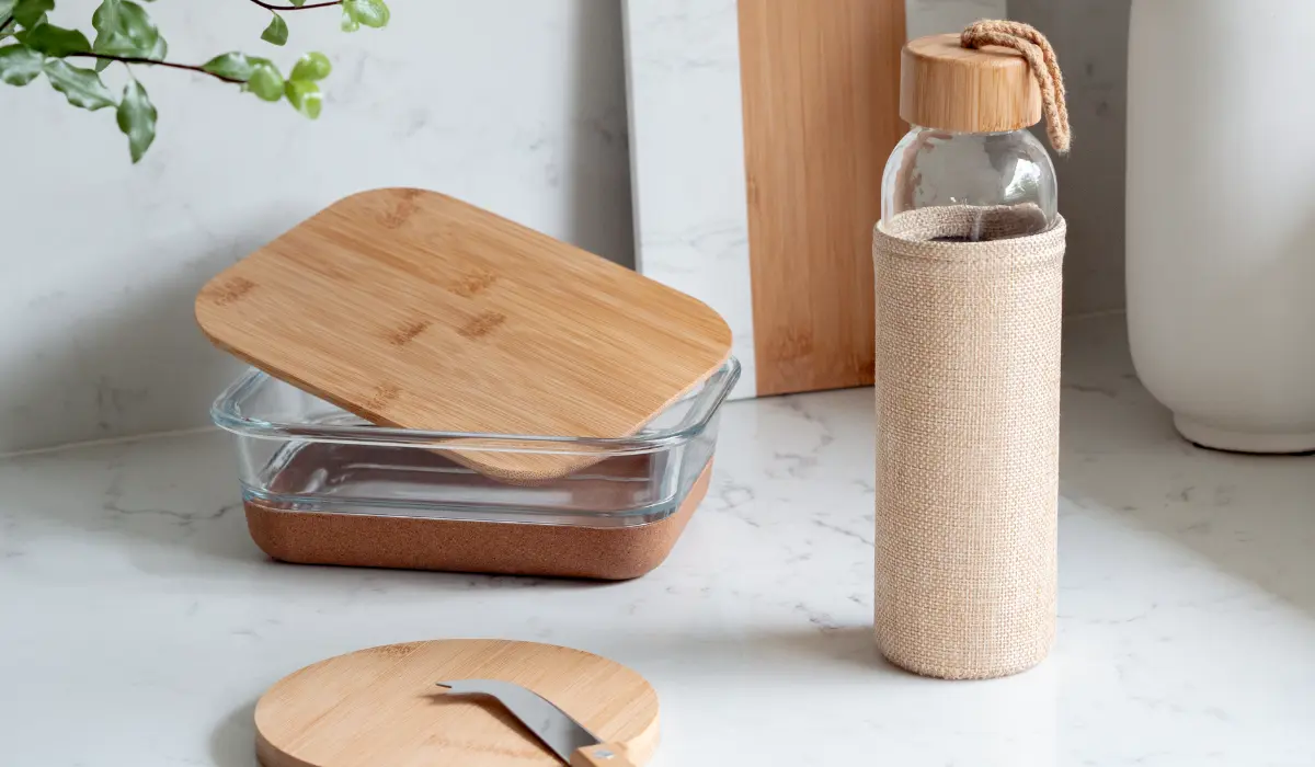 Eco friendly promotional products including a glass food container with bamboo lid and a glass water bottle wrapped in a jute sleeve on a marble surface
