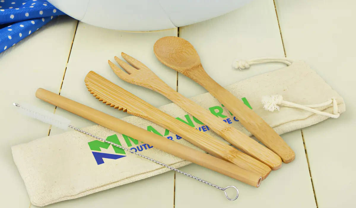 Bamboo cutlery set with fork, knife, spoon, straw, and cleaning brush beside a branded cotton drawstring pouch