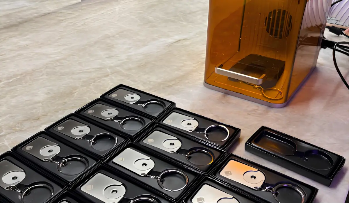 Boxed personalised keyrings laid out beside the live laser engraving machine at an AI brand activation