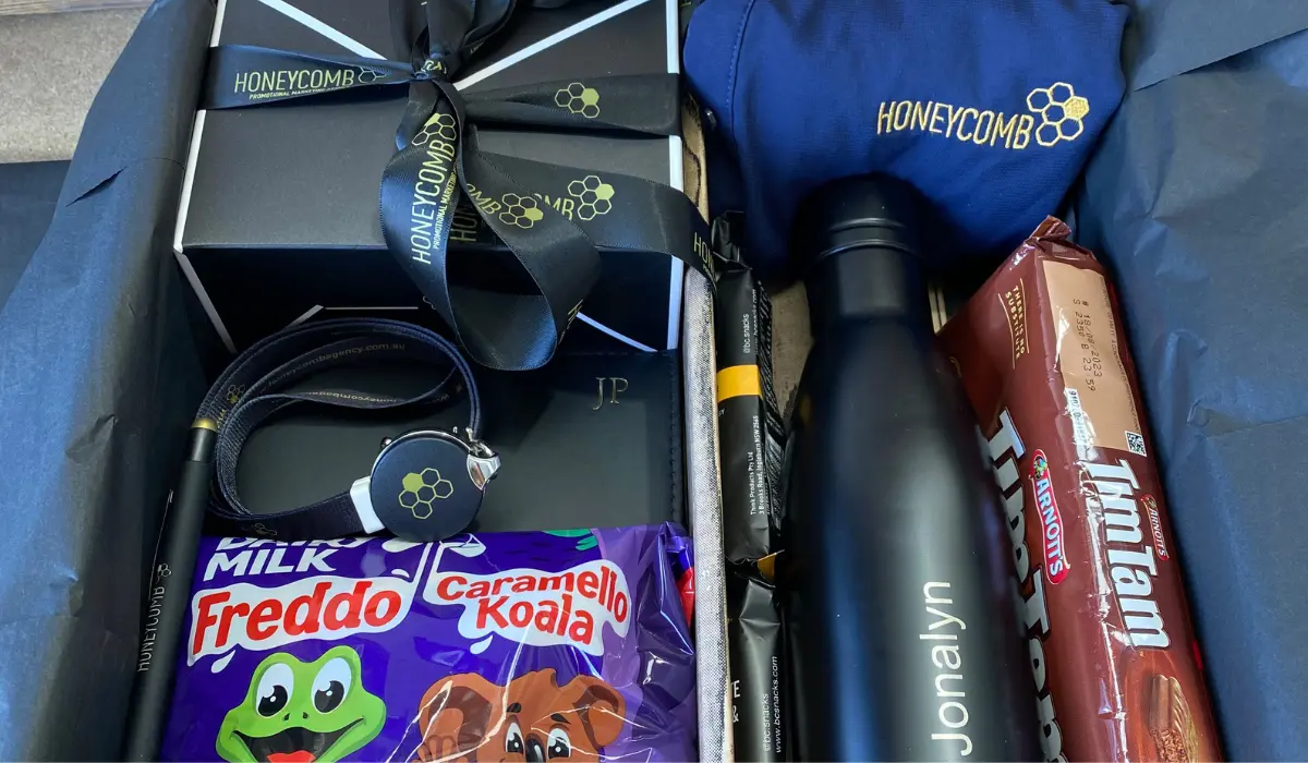 Branded welcome gift box with a Honeycomb-logo jacket and water bottle, personalized flask, chocolate bars, and a lanyard.