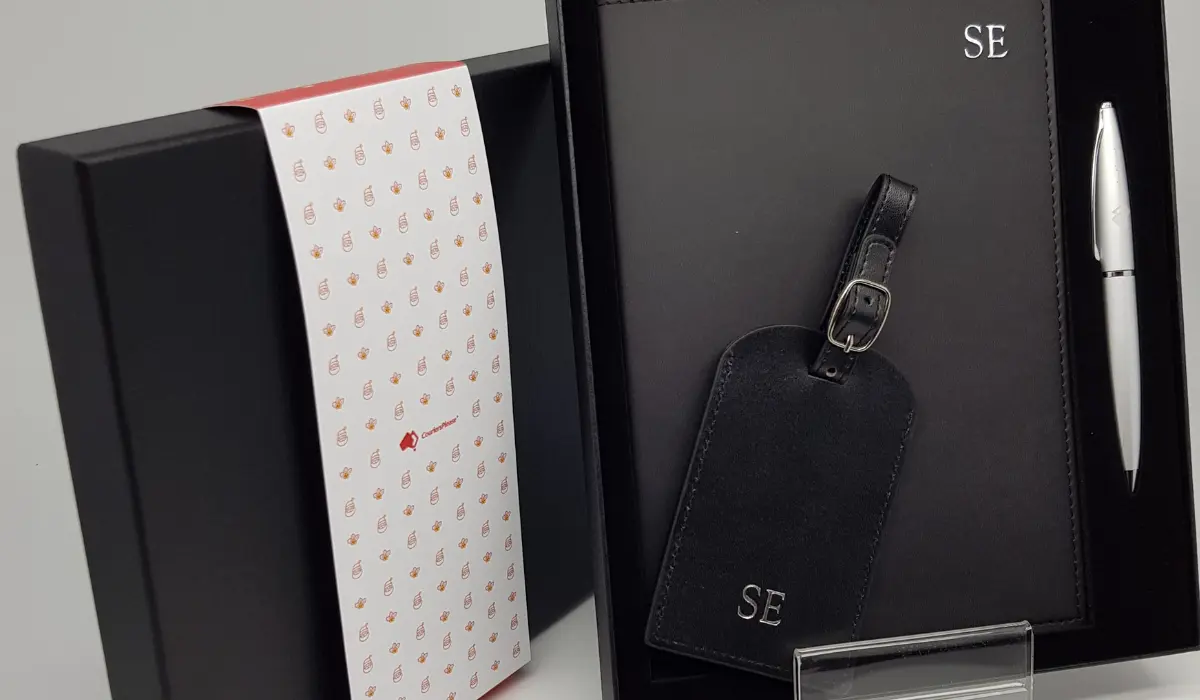 Corporate gift ideas for clients featuring a monogrammed leather luggage tag, silver pen, and notebook in a black gift box.