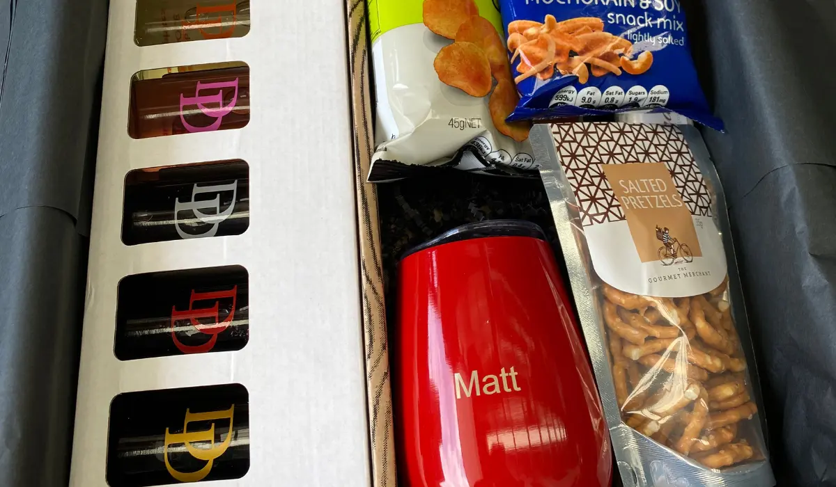 Corporate gift ideas for clients featuring a personalized red tumbler, gourmet pretzels, snacks, and a branded gift box.