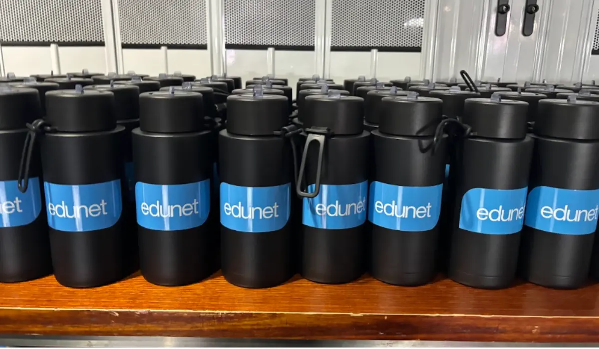 Rows of black branded drink bottles printed with the blue Edunet logo lined up on a timber bench