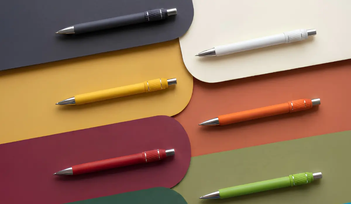 Branded promotional pens in black, white, yellow, orange, red and green laid out on a colour-blocked paper background