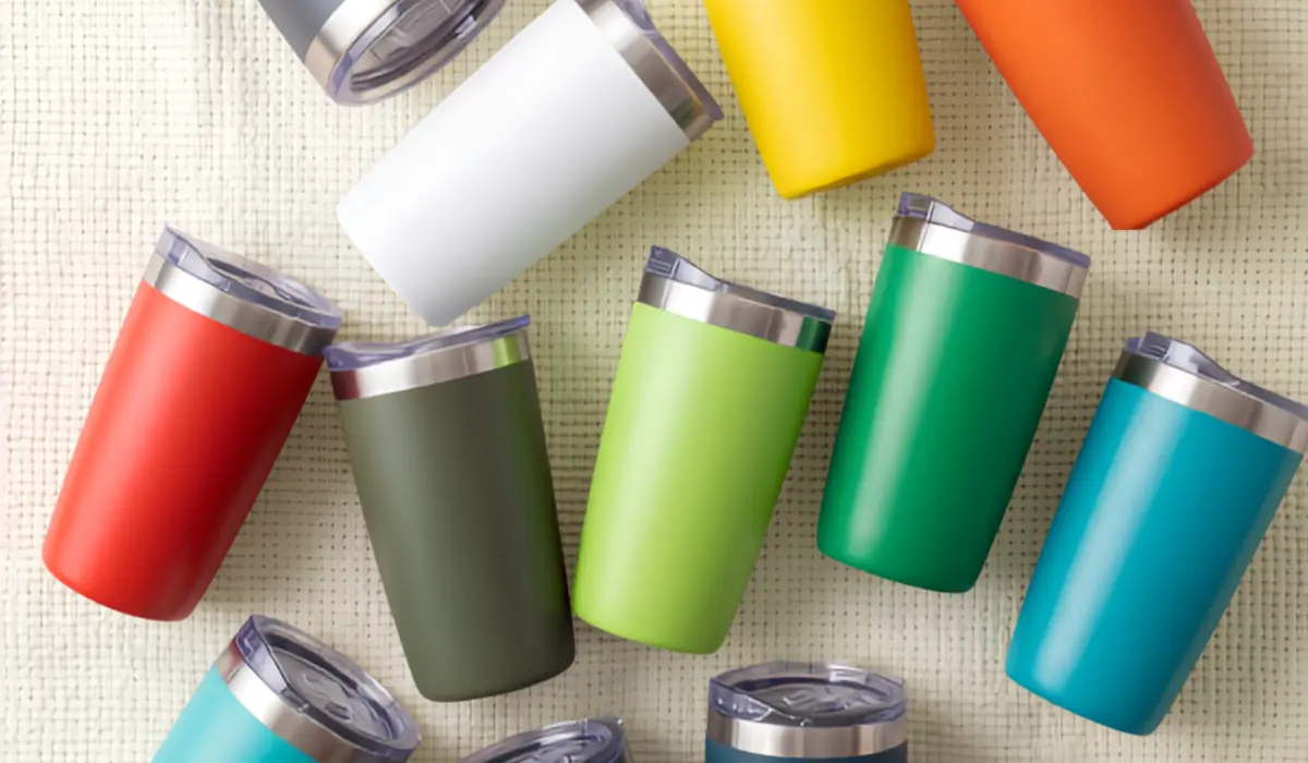 Insulated travel tumblers with clear lids in red, white, olive, lime, green, teal, yellow and orange on a woven surface